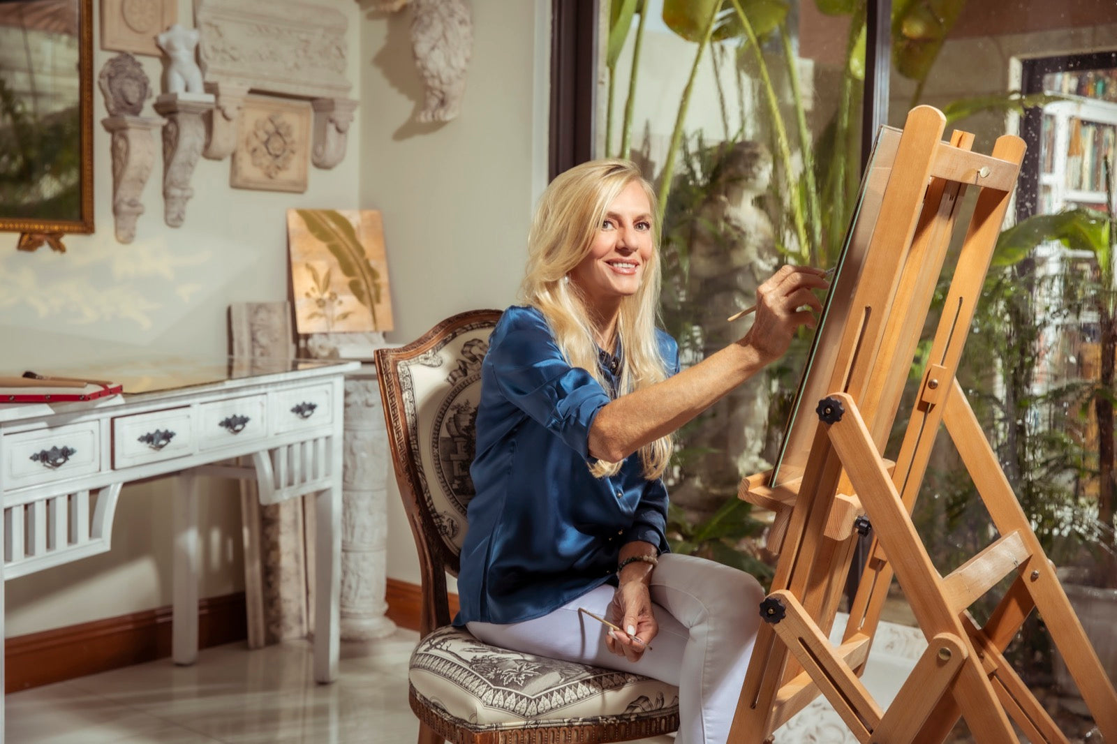 Kim Delaney painting at an easel in her light-filled Florida studio
